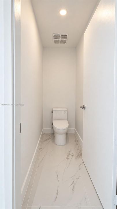 Minimalist water closet featuring large-format porcelain tile flooring with marble-style veining, a high-efficiency toilet, and recessed lighting