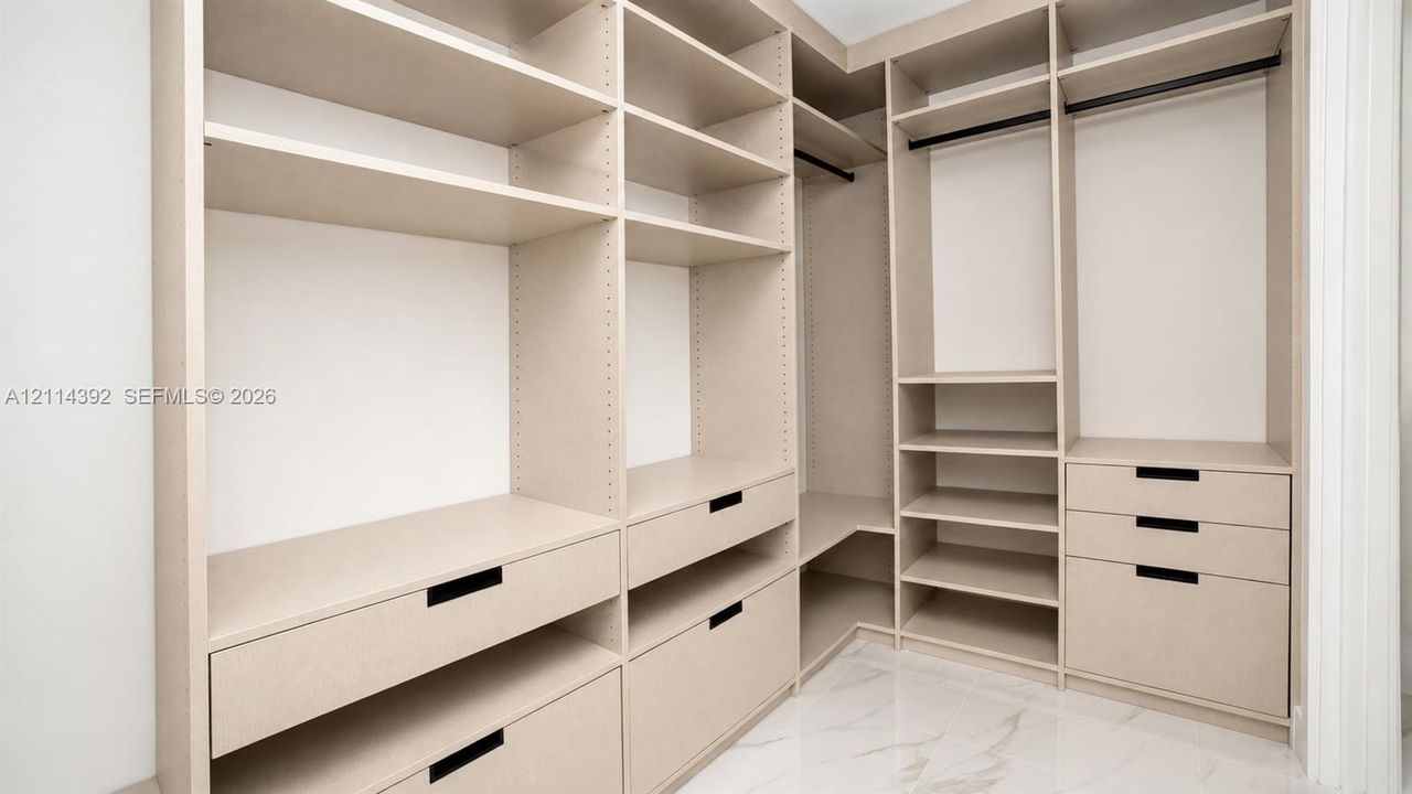 Custom walk-in closet featuring extensive built-in shelving, multiple integrated drawers with matte black pulls, dual hanging rods, and stone-finish flooring