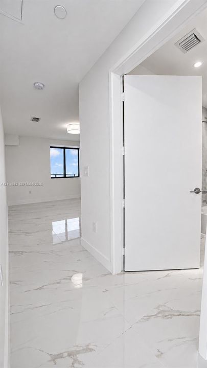 Large-format stone-finish tile flooring, minimalist solid-core interior door, and recessed lighting