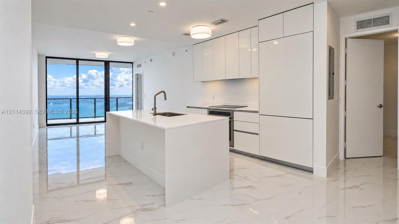 Modern kitchen featuring white flat-panel cabinetry, integrated appliances, a central island with a quartz countertop, and large-format porcelain tile flooring