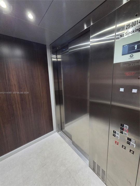 Elevator cab featuring stainless steel doors and control panel, wood-finish wall paneling, and recessed ceiling lighting