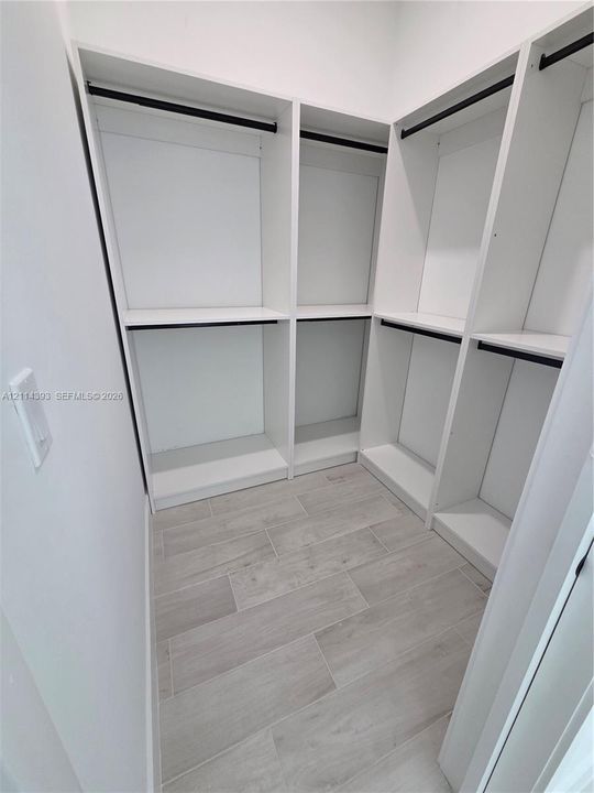 Custom white built-in shelving, integrated hanging rods, and wood-finish tile flooring