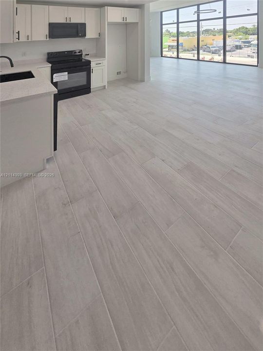 Kitchen featuring white shaker-style cabinetry, solid-surface countertops, black integrated appliances, and wood-finish flooring, accented by floor-to-ceiling windows