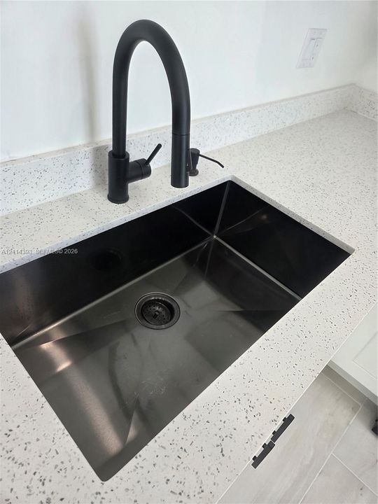 Undermount stainless steel sink featuring a matte black high-arc gooseneck faucet paired with a speckled stone-finish countertop
