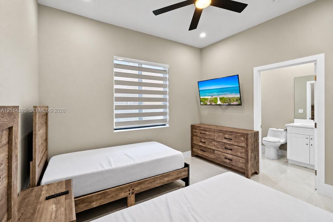 High-ceilinged room featuring a ceiling fan, neutral wall tones, large-format tile flooring, and a window with motorized dual-layer shades