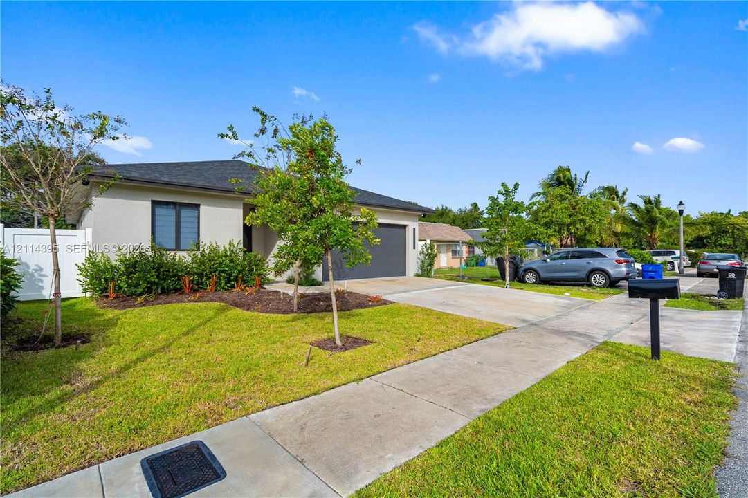 Single-story exterior featuring a light-toned stucco facade, a dark-toned asphalt shingle roof, an attached garage, a concrete driveway, and white privacy fencing