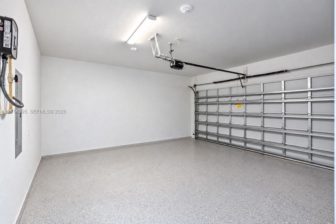 Garage space featuring epoxy-coated flooring, smooth white walls, an automated door opener, and overhead fluorescent lighting