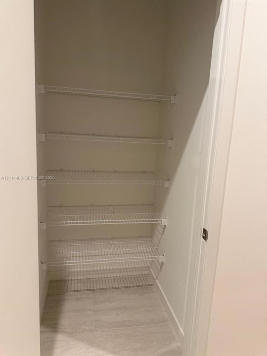 Storage space featuring five tiers of white wire shelving and tile flooring