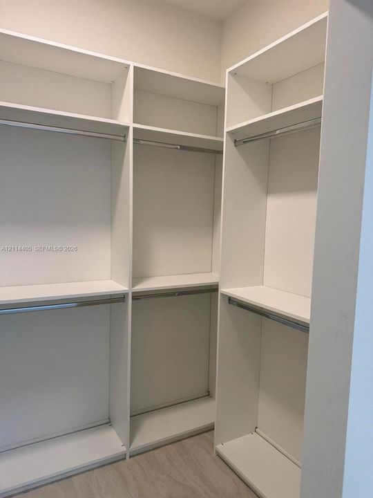 Walk-in closet featuring white built-in shelving, multiple open storage compartments, and metal hanging rods