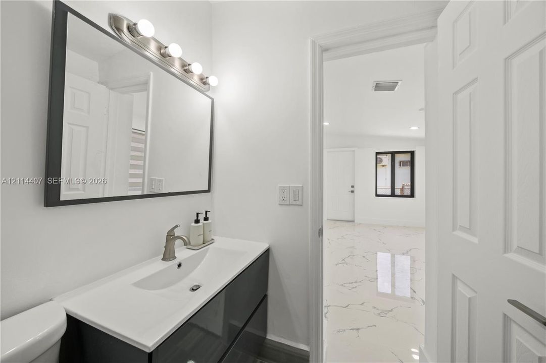 Modern floating vanity with a white integrated basin, polished metal faucet, rectangular framed wall mirror, and vanity light fixture, featuring polished white tile flooring with dark veining