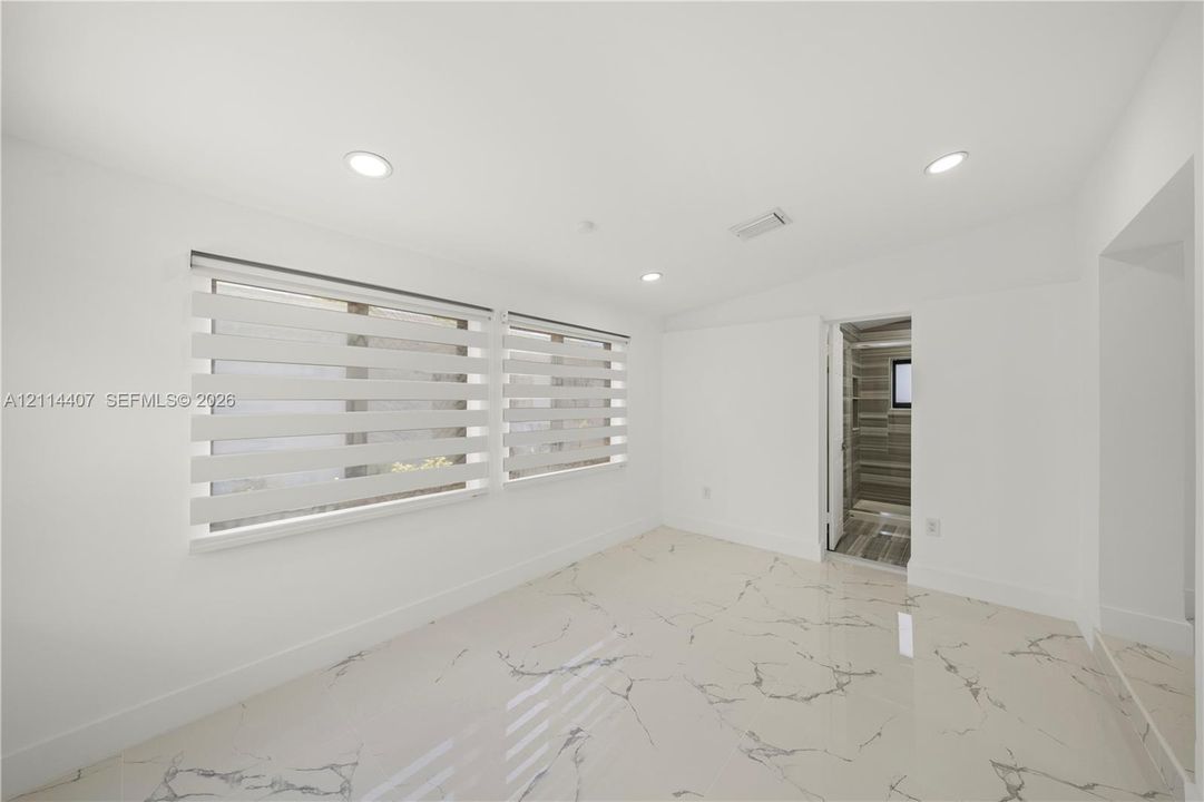Polished stone flooring with veining, recessed lighting, and dual windows featuring horizontal banded shades
