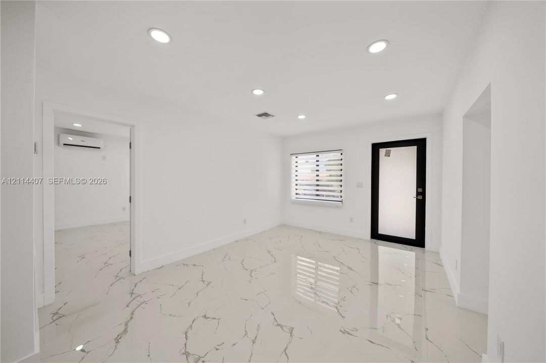 Large-format tile flooring with marble-style veining, recessed lighting, wall-mounted ductless climate control system, and a black-framed entry door with frosted glass panel