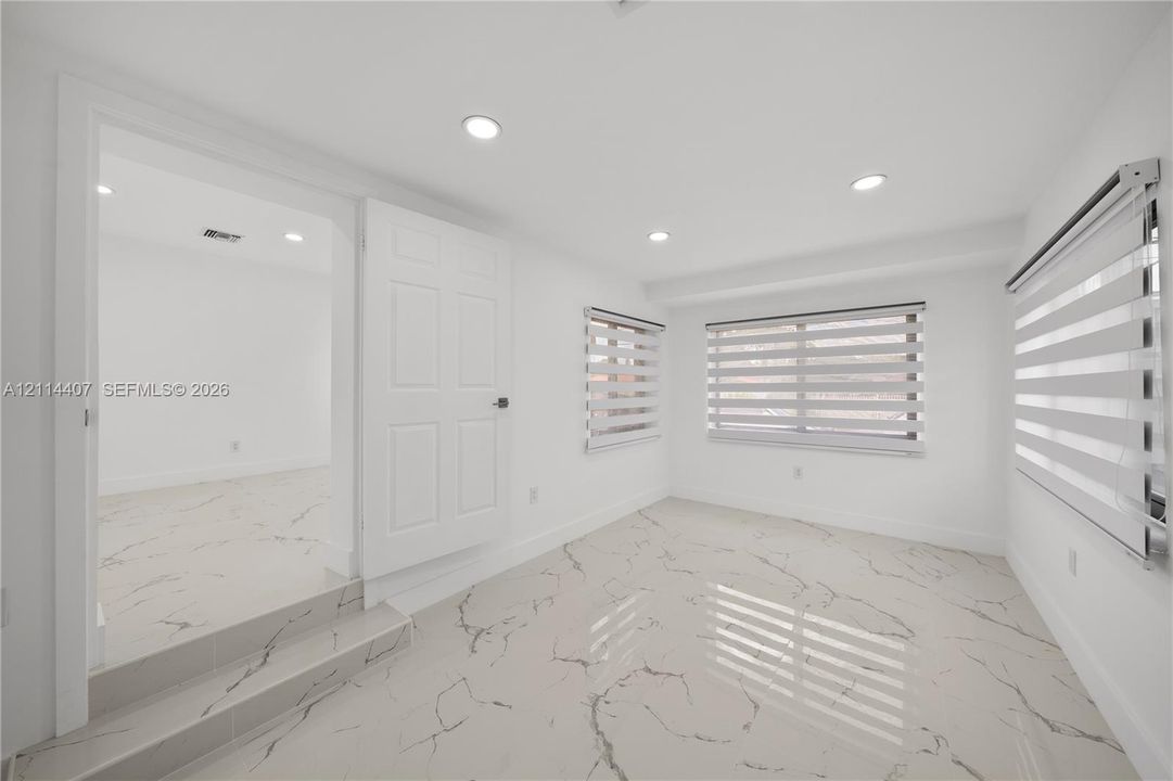 Interior space featuring stone-style tile flooring with veining, recessed lighting, multi-panel doors, and horizontal zebra-style window treatments