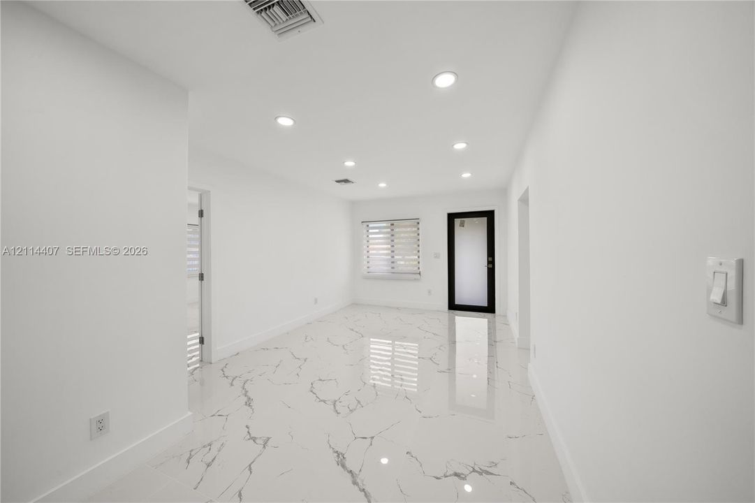Polished stone-finish flooring with veining detail, recessed lighting, and an exterior door with a glass inlay