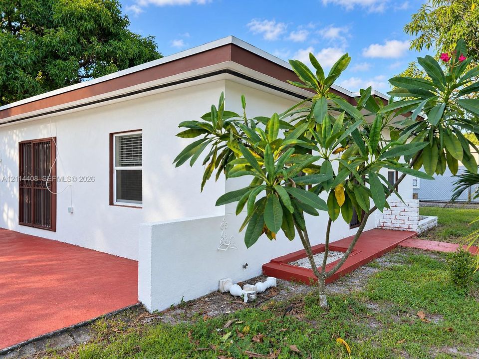 Exterior featuring painted masonry walls, flat roofline, red-finished concrete patio, sliding glass doors with metal security screen, and white masonry perimeter wall
