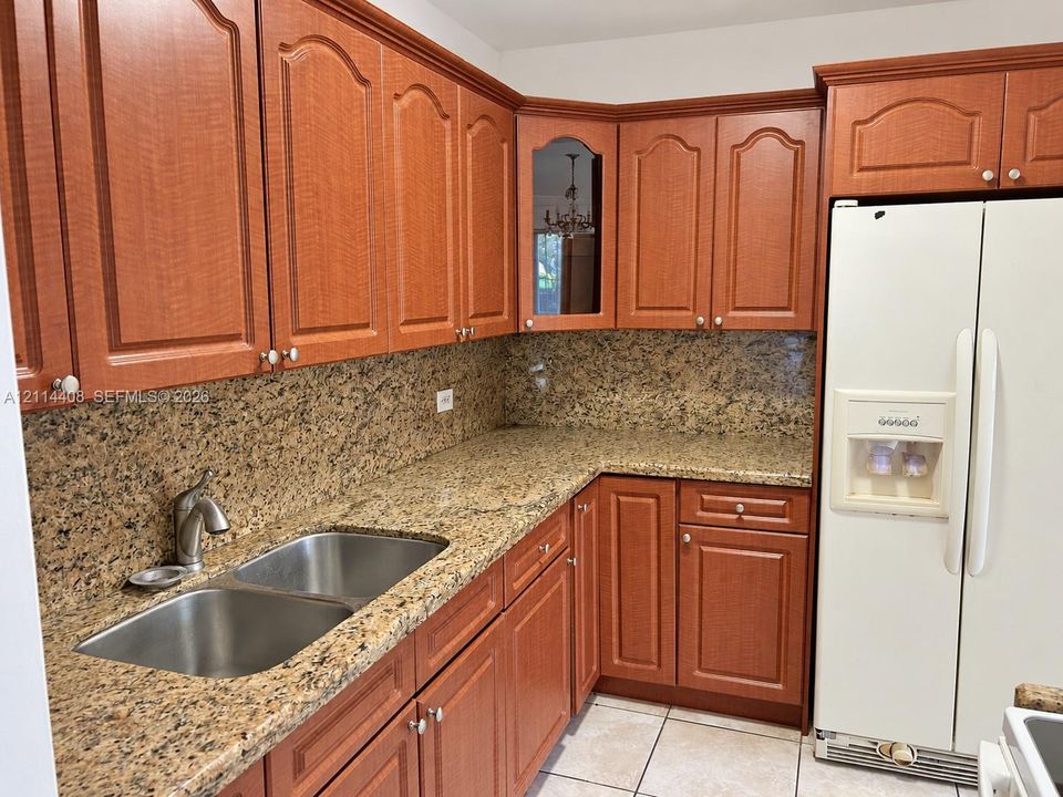 Kitchen featuring wood cabinetry with arched detailing, natural stone countertops, a full-height stone backsplash, a stainless steel double-basin undermount sink, and a glass-front display cabinet