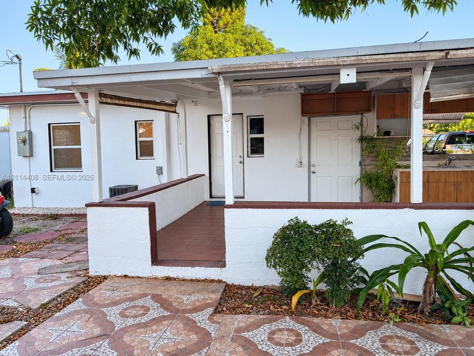 Exterior facade featuring a covered patio, tile flooring, masonry knee walls, and an outdoor kitchen area with wooden cabinetry