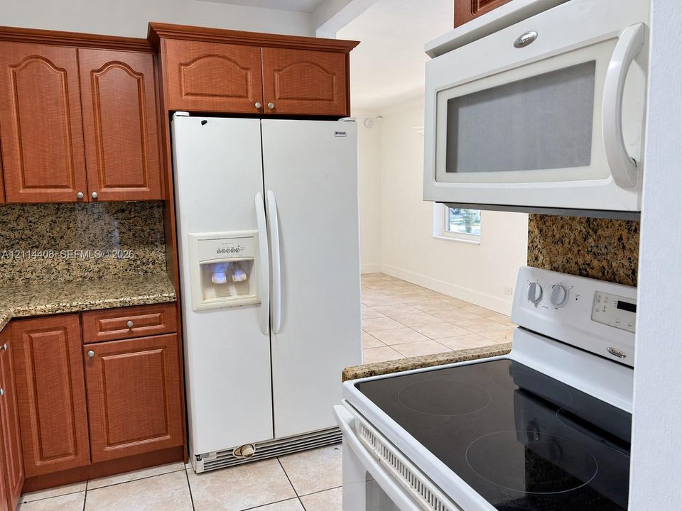 Kitchen featuring stained wood cabinetry, stone-finish countertops, tile flooring, and integrated white appliances including a side-by-side refrigerator, over-the-range microwave, and electric cooktop