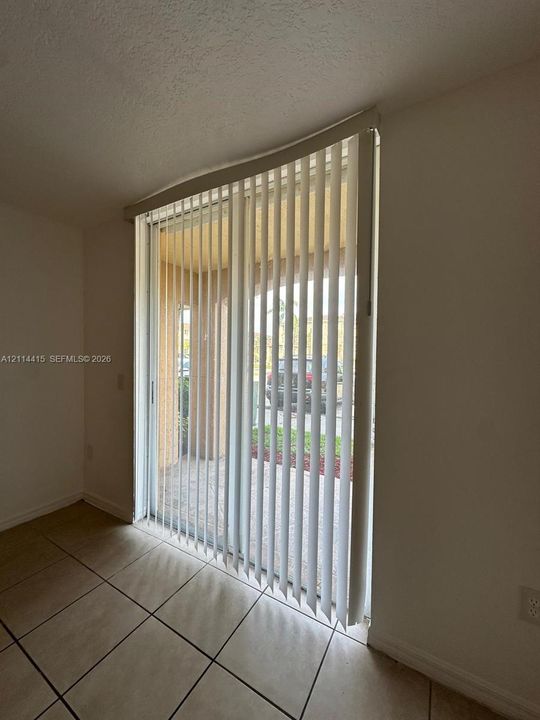 Sliding glass door with vertical blinds, tile flooring, and access to a paved patio area