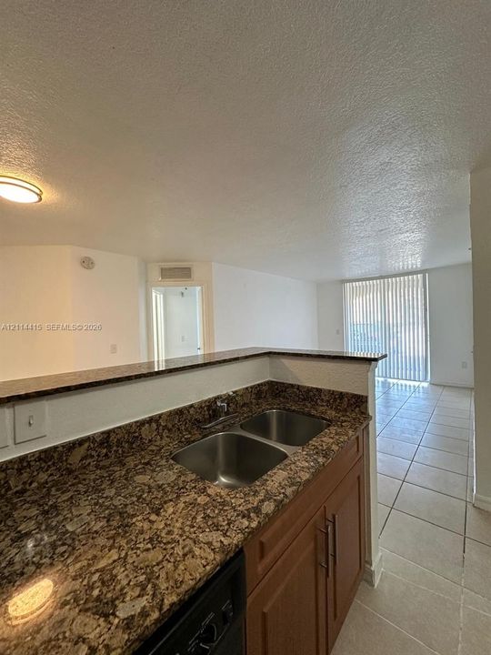 Kitchen featuring stone-finish countertops, dual-basin stainless steel sink, wood-finish cabinetry with bar-pull hardware, and light-toned tile flooring