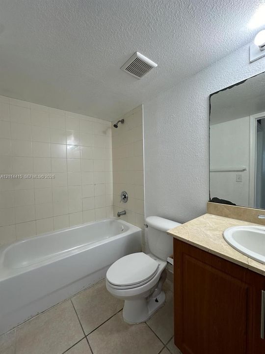 Bathroom featuring a shower-tub combination with tiled surround, wood-finish cabinetry, stone-surface countertop, and a recessed mirror