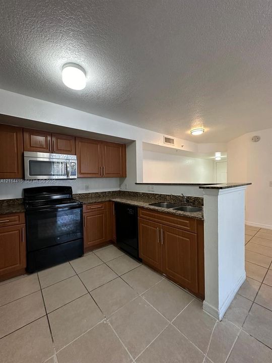 Kitchen featuring wooden cabinetry, stone-surface countertops, dual-basin sink, integrated black appliance suite, and tile flooring