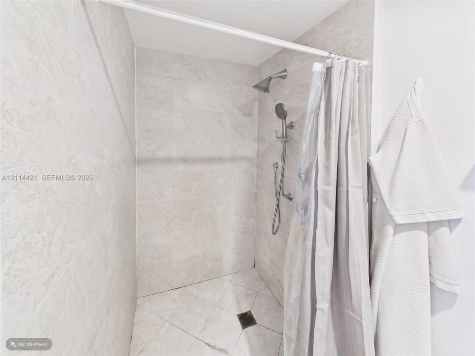 Walk-in shower featuring floor-to-ceiling stone-finish tile, diamond-patterned tile flooring, a dual-head shower system with a handheld sprayer, and a tension-mounted shower rod