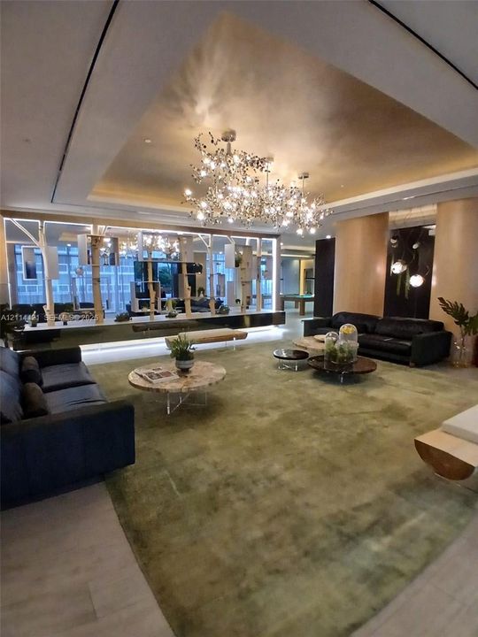 Expansive living space featuring a recessed tray ceiling, a custom branching chandelier, floor-to-ceiling glass wall panels with structural framing, and wood-finish flooring