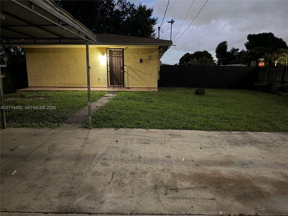 Stucco exterior featuring an attached metal carport, concrete driveway, and enclosed backyard with privacy fencing