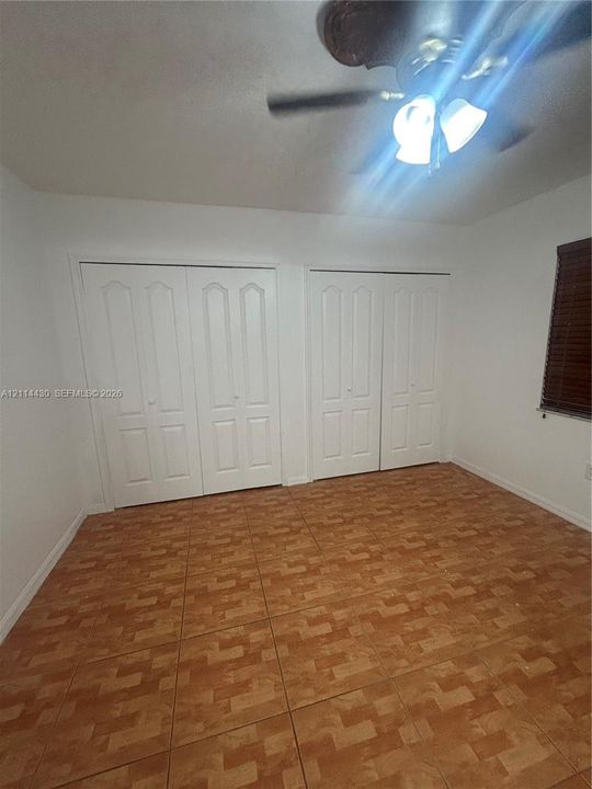 Room featuring tile flooring, two sets of white panel doors with built-in closet storage, and a ceiling fan with integrated lighting