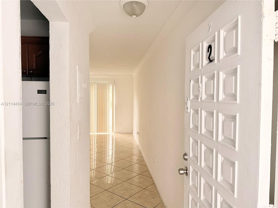 Entryway featuring a white paneled door, neutral-toned tile flooring, and sliding vertical blinds