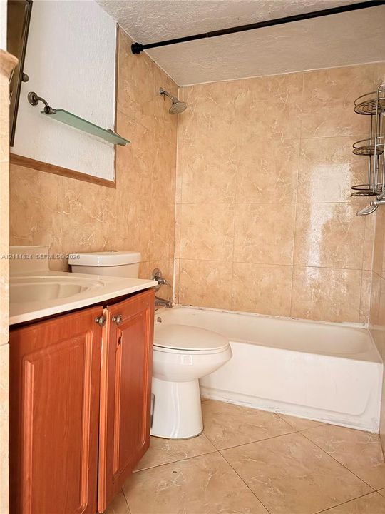 Bathroom featuring wood-finish vanity cabinetry, a solid-surface countertop with an integrated sink, full-height tile wall surrounds, and tile flooring