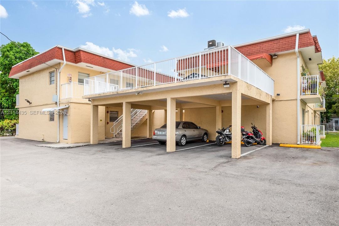 Multi-story exterior featuring a covered parking structure, metal staircase, and an upper-level balcony with metal railings