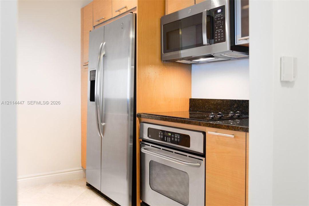Kitchen featuring light wood-finish cabinetry, stainless steel side-by-side refrigerator, built-in electric wall oven, glass cooktop, and stainless steel microwave