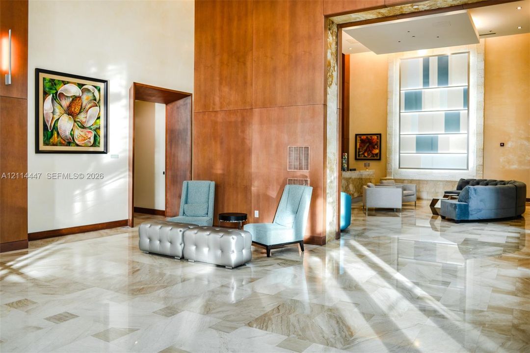 Grand foyer featuring polished stone flooring, floor-to-ceiling wood paneling, recessed tray ceilings, and an oversized rectangular window feature