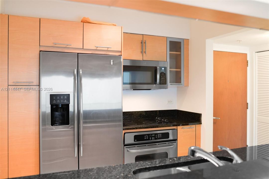 Kitchen featuring light-finish cabinetry, dark stone countertops, stainless steel appliances, and a glass-paneled upper cabinet door