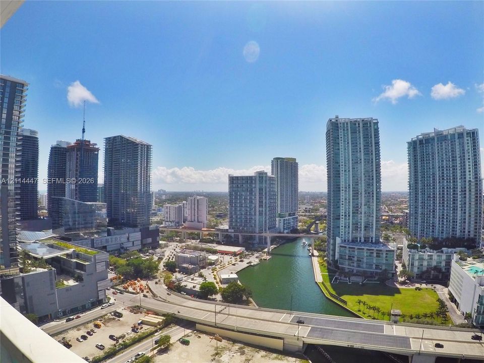 High-rise perspective featuring expansive glass-clad skyscrapers, a canal, and elevated transportation infrastructure