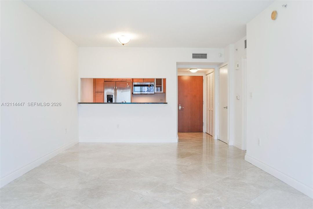 Open-concept interior featuring light-toned stone tile flooring, pass-through kitchen opening with dark countertop, stainless steel refrigerator, built-in microwave, and solid wood-finish entry door