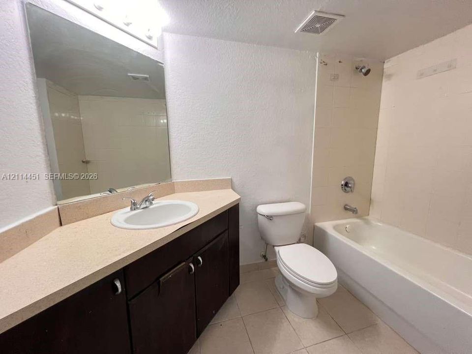 Bathroom featuring dark wood-finish cabinetry, light-toned solid surface countertop with integrated sink, full-width wall mirror, tile flooring, and a tub-shower combination with tile surround