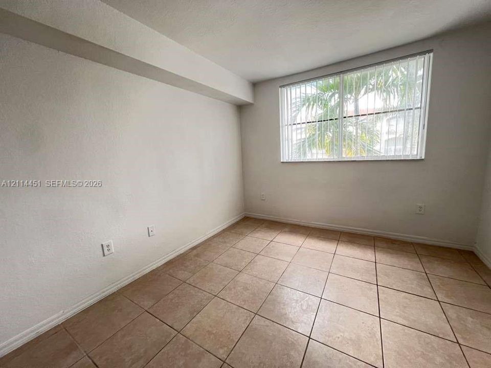 Neutral-toned interior space featuring light-colored tile flooring and a horizontal window fitted with vertical blinds
