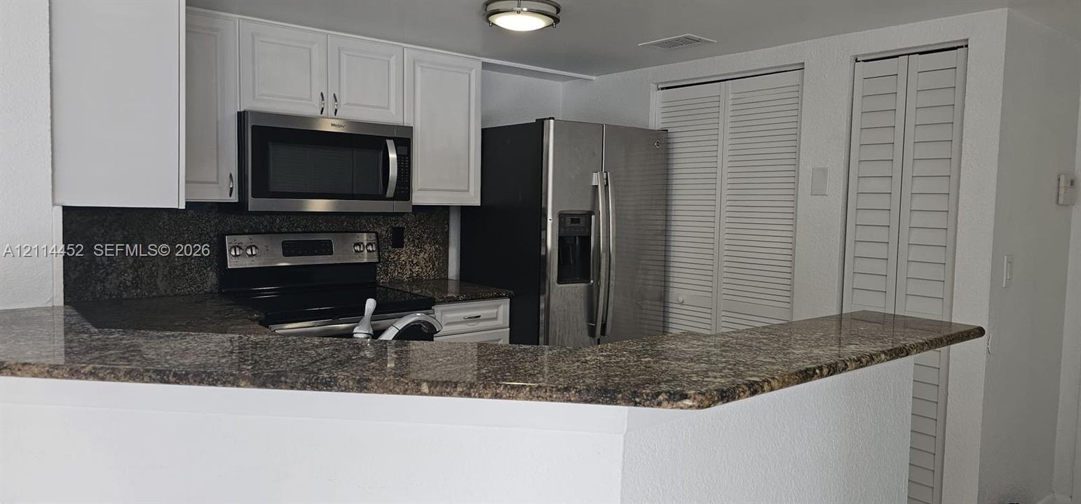 Kitchen featuring white cabinetry, stone countertops, stainless steel appliances, and louvered-style closet doors