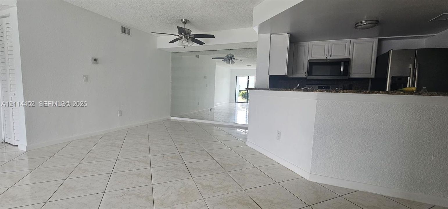 Open-concept interior featuring diagonal tile flooring, white cabinetry, dark stone-finish countertops, built-in ceiling fans, and a full-height wall mirror