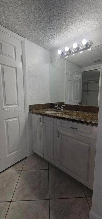 Vanity featuring a stone countertop with an integrated basin, white cabinetry, a large wall-mounted mirror, and tile flooring