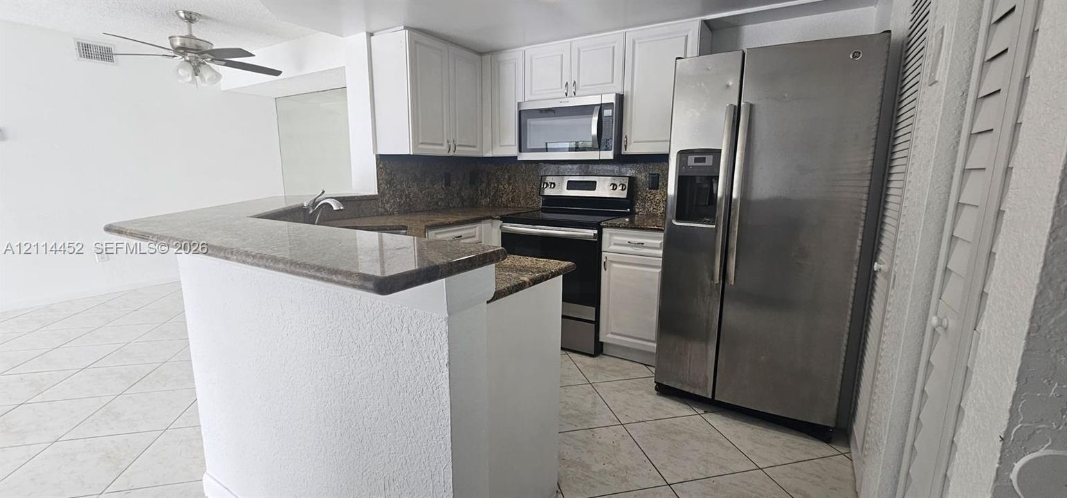Kitchen featuring white shaker-style cabinetry, stone-finish countertops, stainless steel appliances, and tile flooring