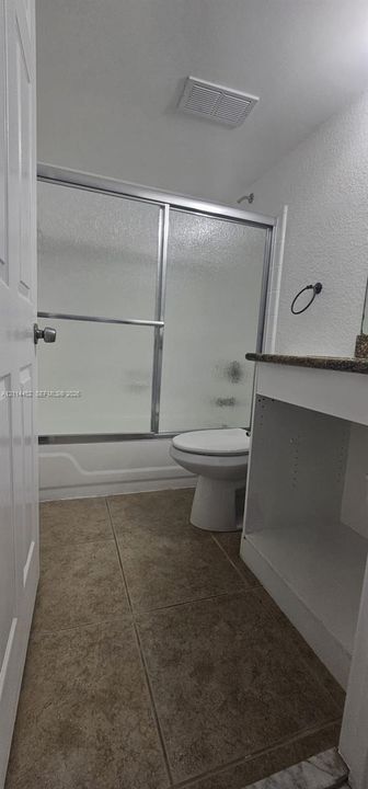 Bathroom featuring tile flooring, a white vanity with a stone-surface countertop, and a shower-tub combination enclosed by sliding glass doors