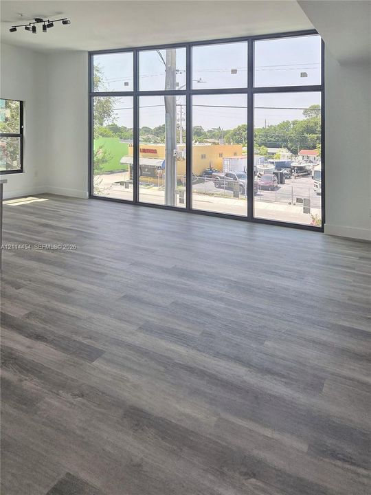 Floor-to-ceiling windows with black frames, wood-finish flooring, and black multi-directional track lighting