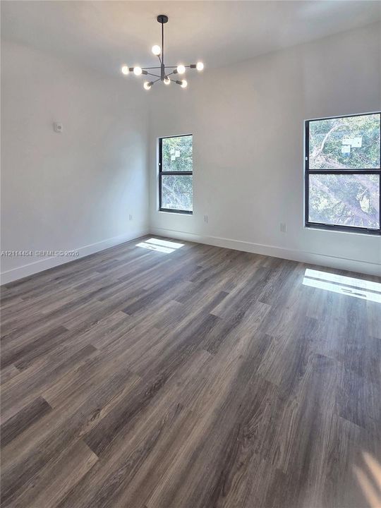 Interior space featuring wood-finish flooring, high ceilings, large windows with dark frames, and a multi-arm modern chandelier