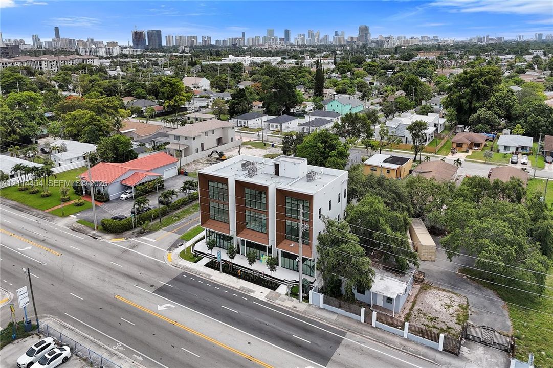 Contemporary three-story structure featuring a concrete facade, wood-finish paneling, expansive floor-to-ceiling windows, a flat roof, and metal balcony railings
