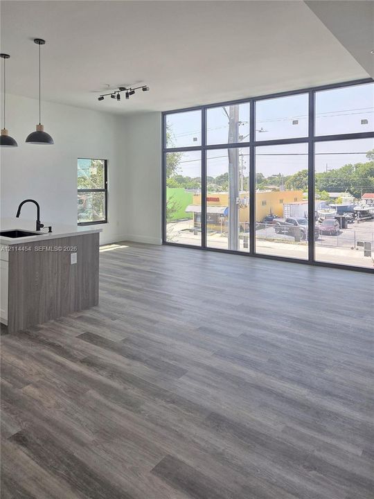 Open-concept interior featuring floor-to-ceiling windows, wood-finish flooring, a kitchen island with a quartz countertop, and black matte pendant lighting