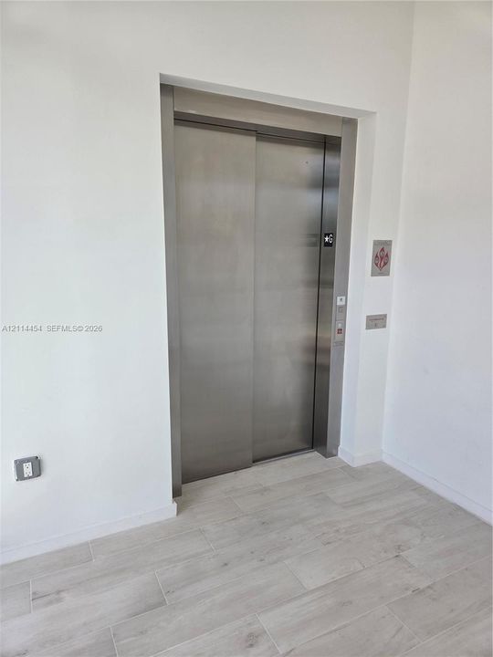 Stainless steel elevator featuring a brushed metal finish and neutral wood-finish flooring